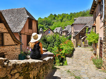 Femme assise sur un muret dans une ruelle de Conques