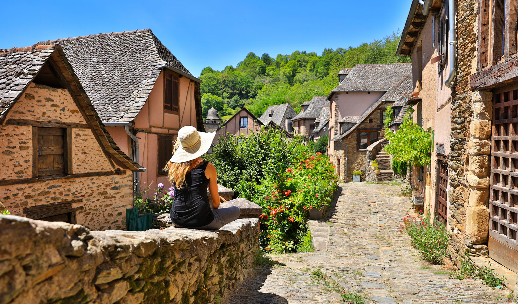 Femme assise sur un muret dans une ruelle de Conques